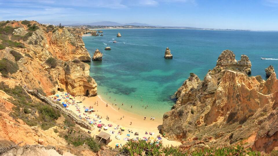 A coastal landscape with a sandy beach, rocky cliffs, and clear blue sea.