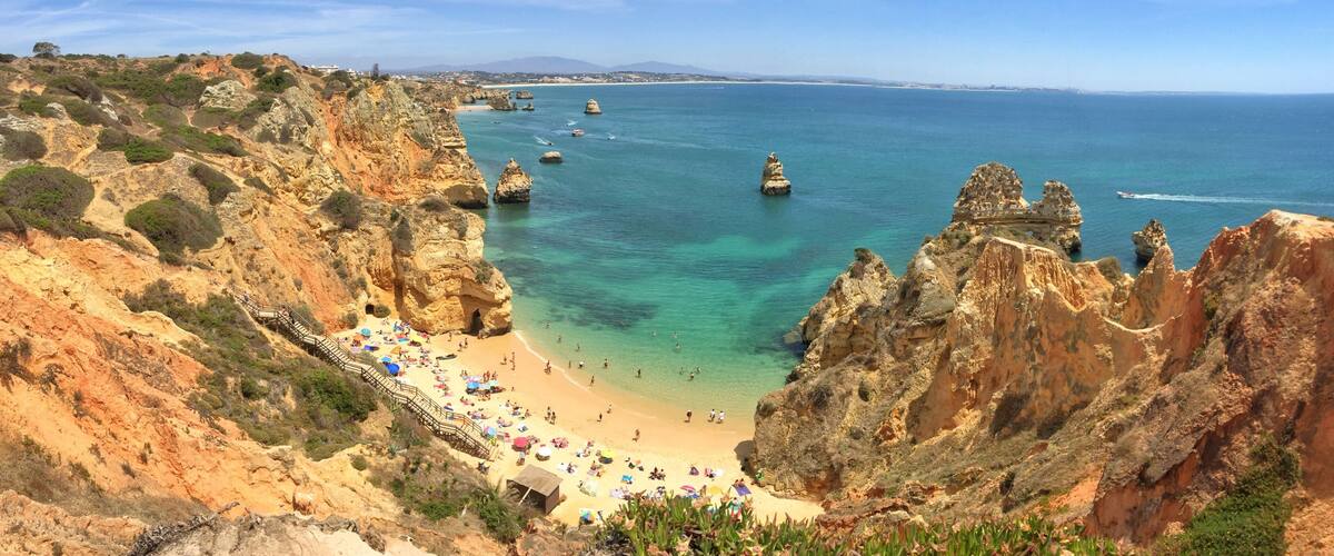 A coastal landscape with a sandy beach, rocky cliffs, and clear blue sea.
