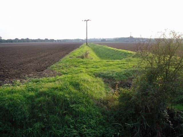 Ditches off Barton Road. A strip of vivid green contrasts with the brown ploughed fields.