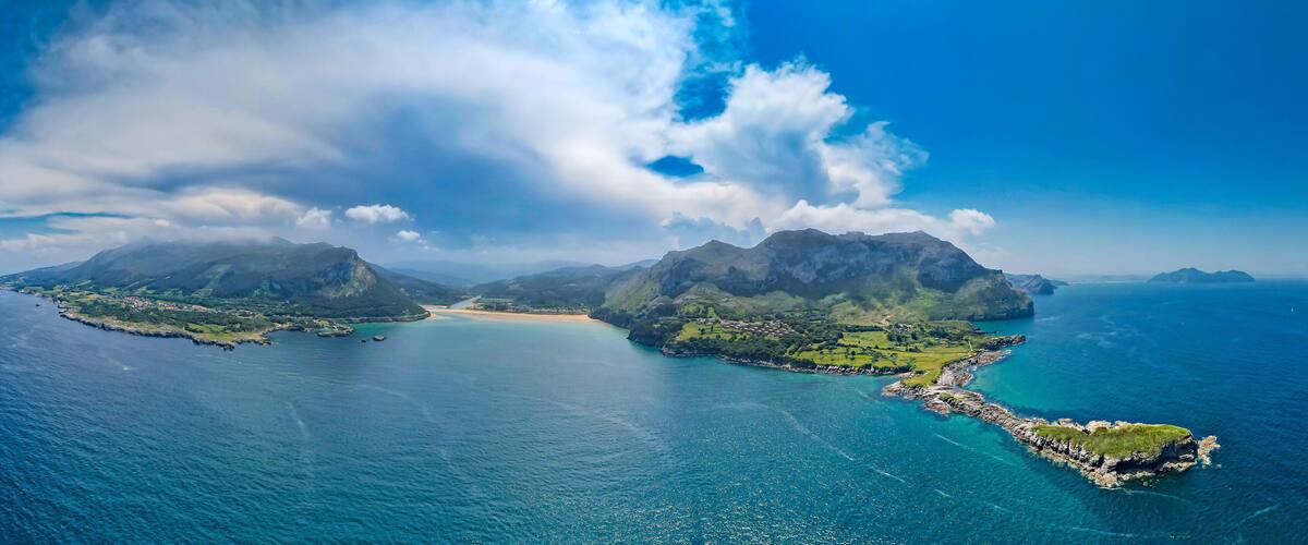 An aerial view of a coastal landscape with two prominent islands, a clear blue sky, and a calm sea.