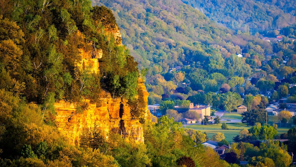 Eine Klippe mit einem Dorf am Fuße, umgeben von dichtem Wald.