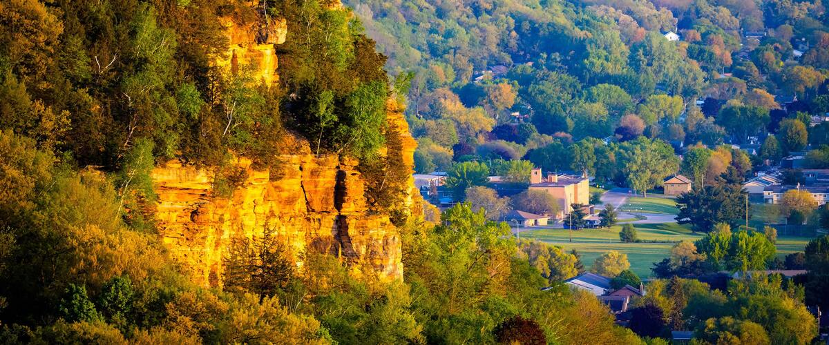 A cliff with a village at its base, surrounded by dense forest.