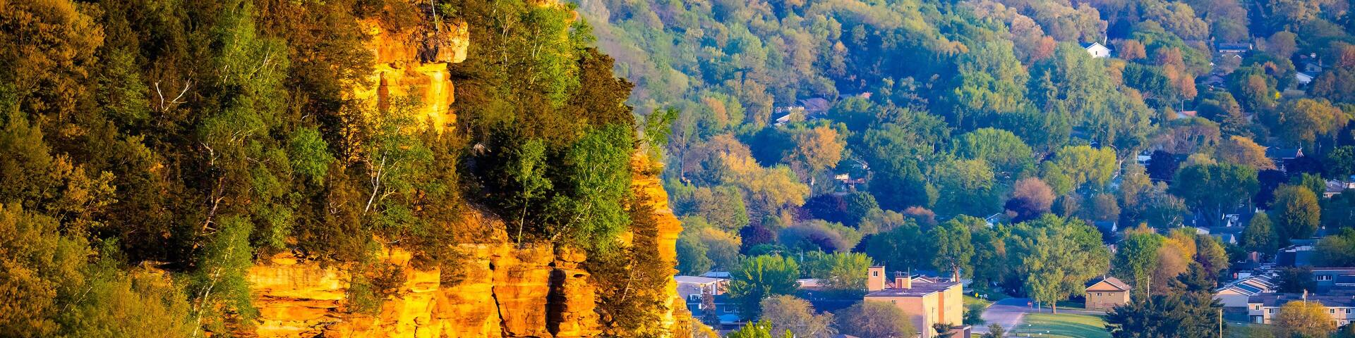 A cliff with a village at its base, surrounded by dense forest.