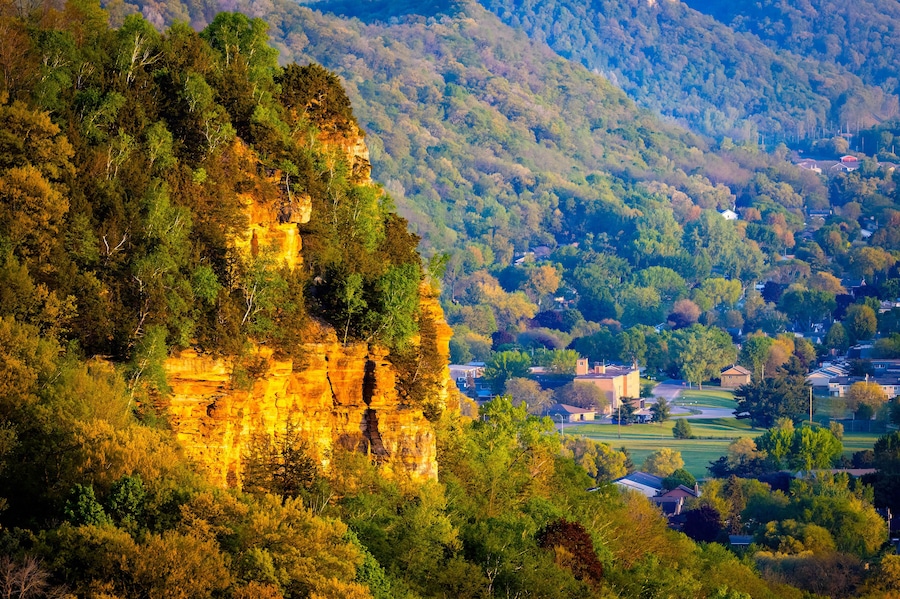 A cliff with a village at its base, surrounded by dense forest.