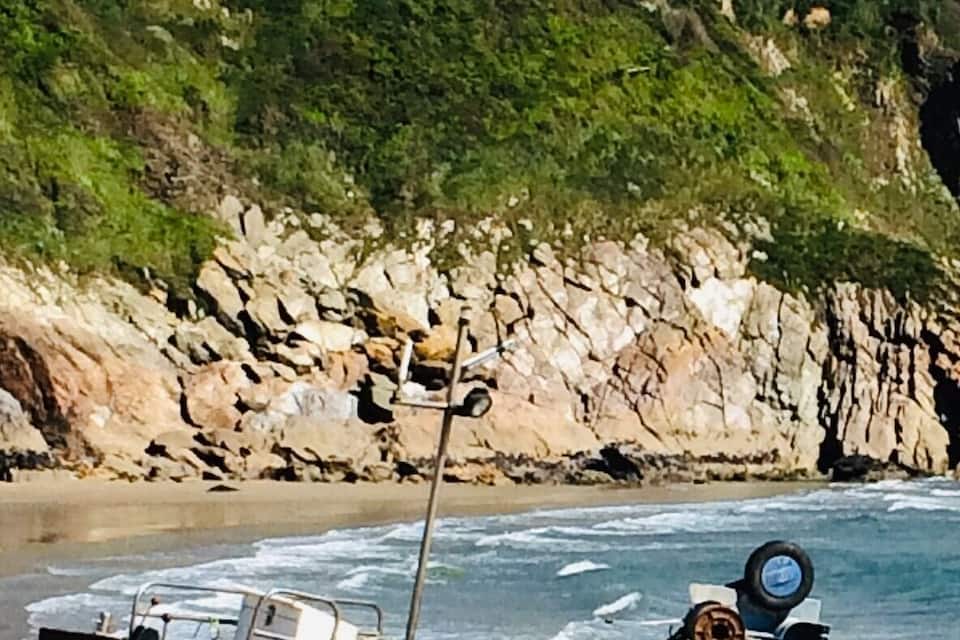 Un vaixell anomenat 'FY1' a una platja sorrenca amb penya-segats rocosos i cases al fons.