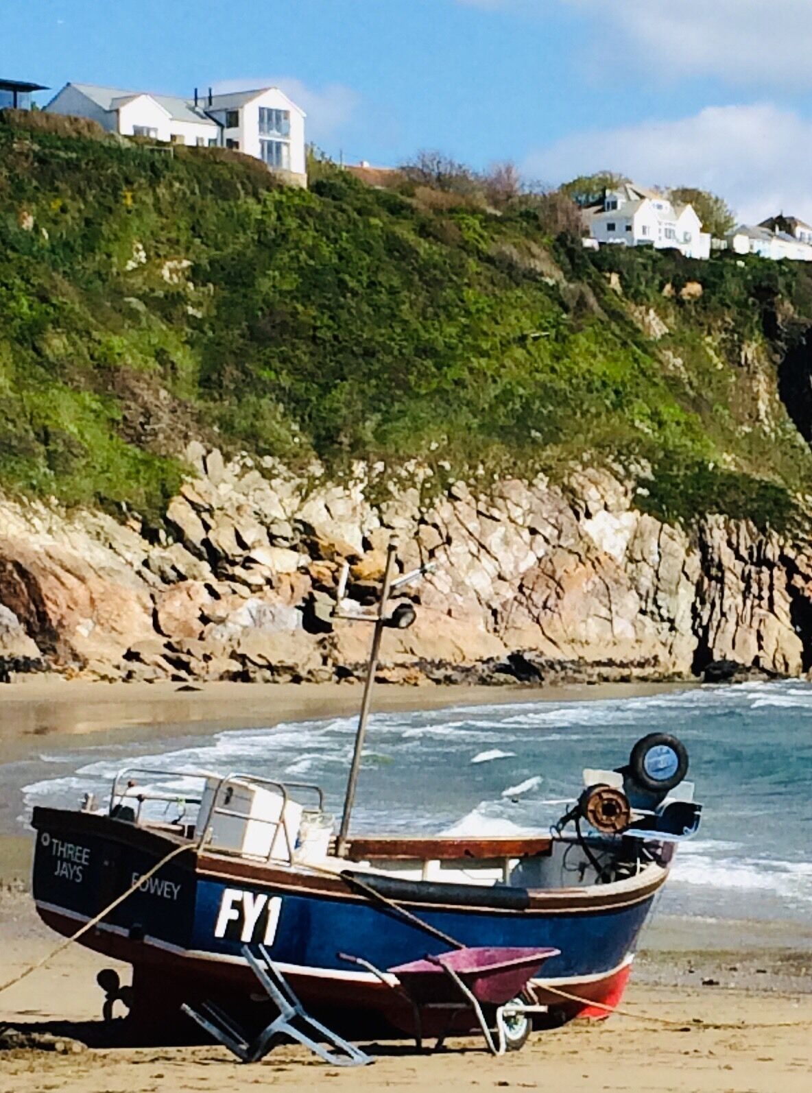 A boat named 'FY1' on a sandy beach with rocky cliffs and houses in the background.