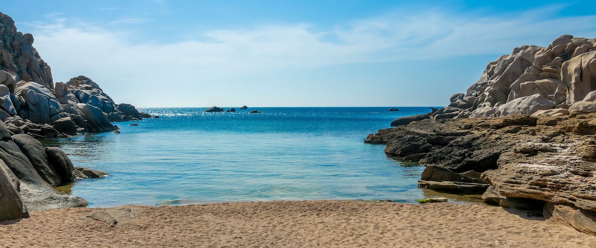 A rocky coastline with clear blue water and distant land.