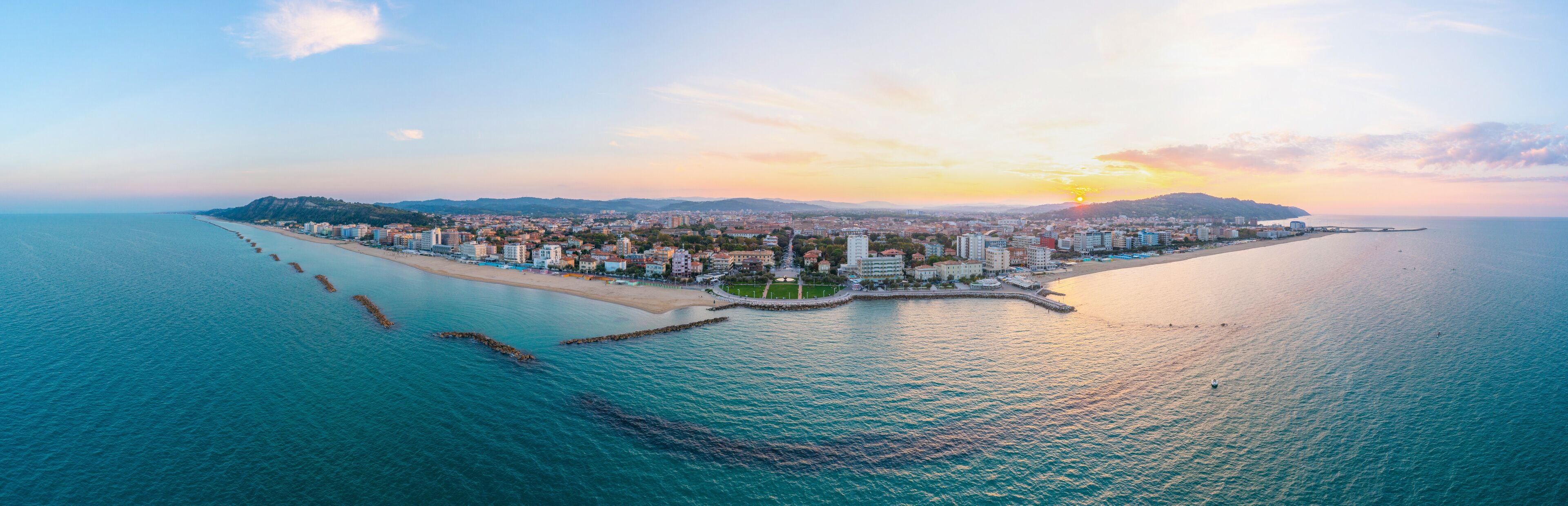 An aerial view of a coastal city with a beach, buildings, and a sunset.