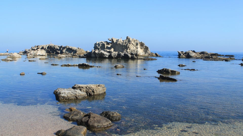 A rocky coastline with clear shallow waters and scattered rocks.