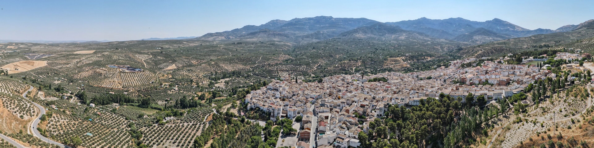 Vista aérea de uma cidade situada num vale, com montanhas e oliveiras ao redor.