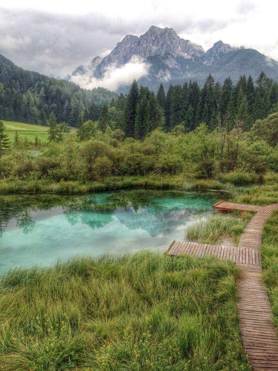 A clear lake surrounded by lush greenery and mountains in the background.