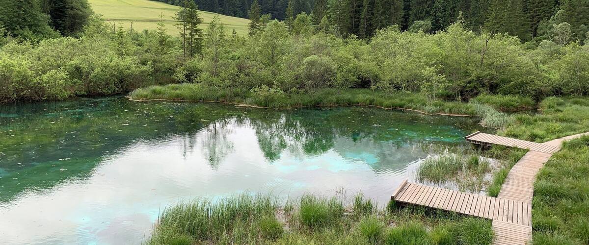 A clear lake surrounded by lush greenery and mountains.