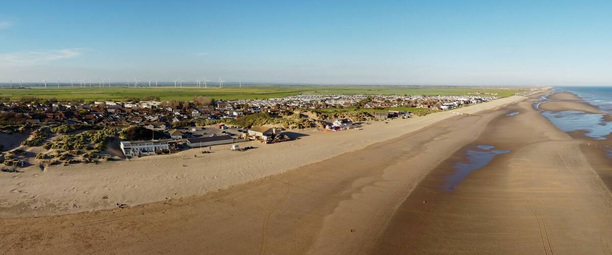 A coastal town with a beach, houses, and wind turbines in the distance.