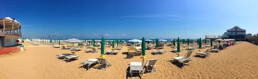 Ein Strand mit Reihen von Liegestühlen und Sonnenschirmen, einem Rettungsturm und einem Gebäude im Wellendesign.