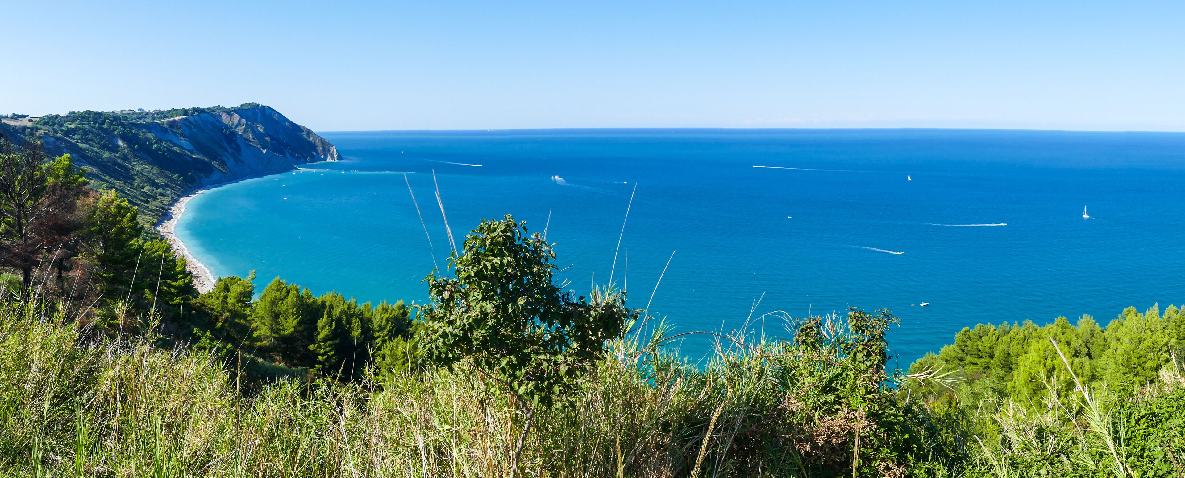 Un paisaje costero con mar azul cristalino, una playa arenosa y colinas verdes.