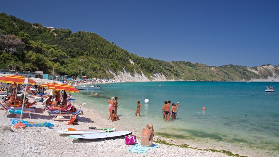 A beach with clear turquoise water, people sunbathing, and boats.