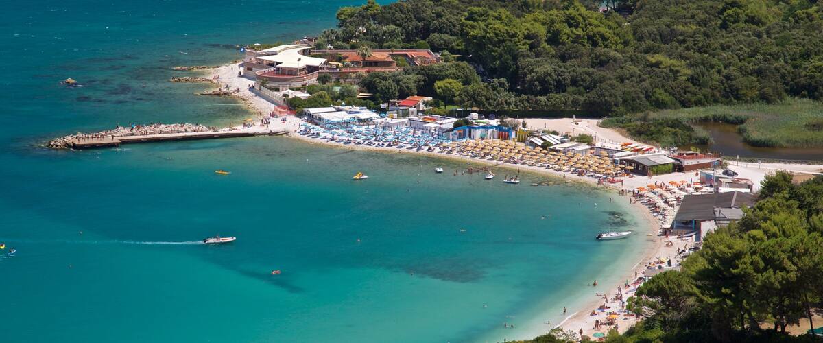 A coastal town with a beach, boats, and a forested hill.