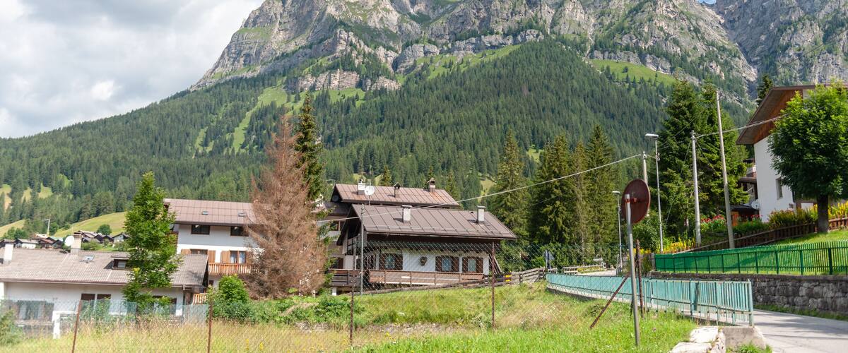 A mountain landscape with a house and a green fence in the foreground.