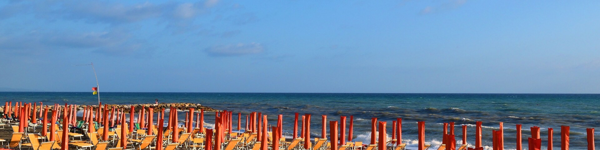 Uma praia com fileiras de cadeiras de praia e guarda-sóis laranja.