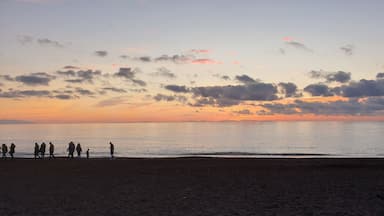A beach at sunset with silhouettes of people walking along the shore.