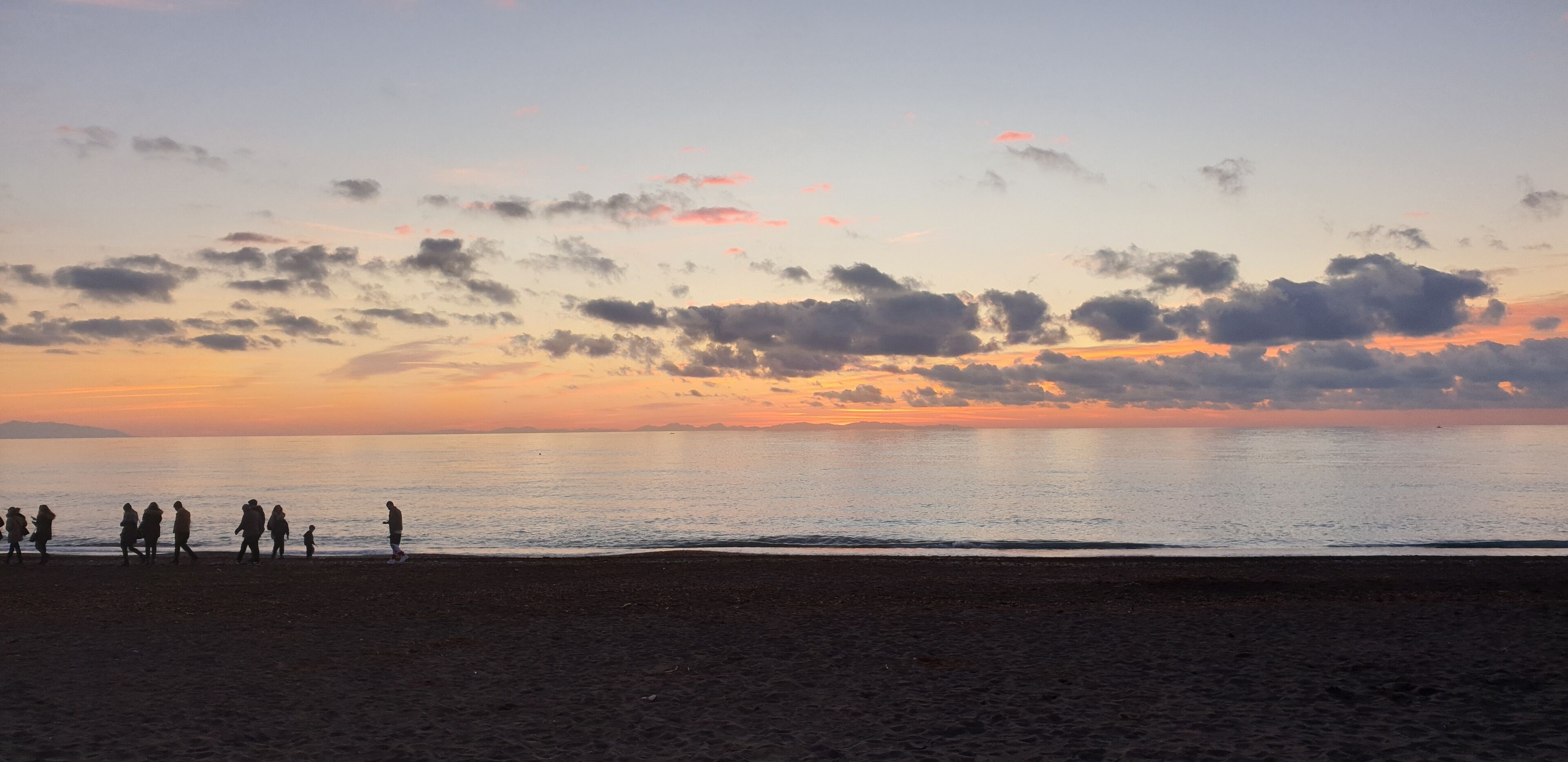 A beach at sunset with silhouettes of people walking along the shore.