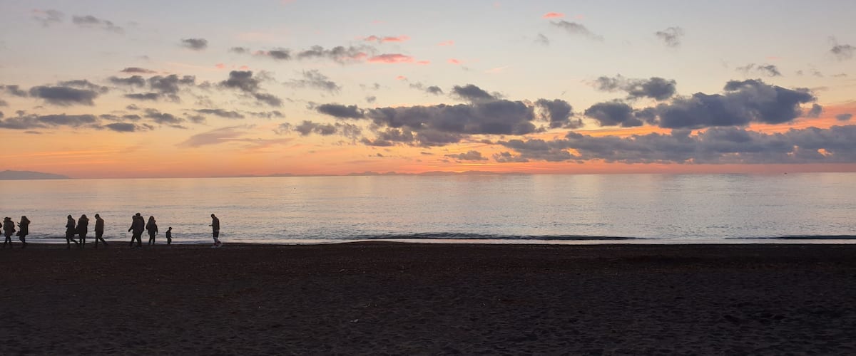 A beach at sunset with silhouettes of people walking along the shore.