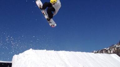 A snowboarder mid-air performing a jump over a snow ramp.