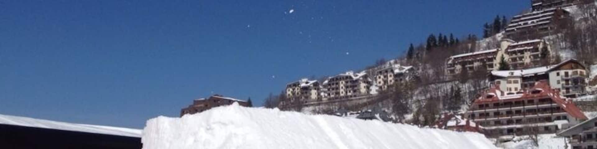 A snowboarder mid-air above a snow ramp with buildings in the background.