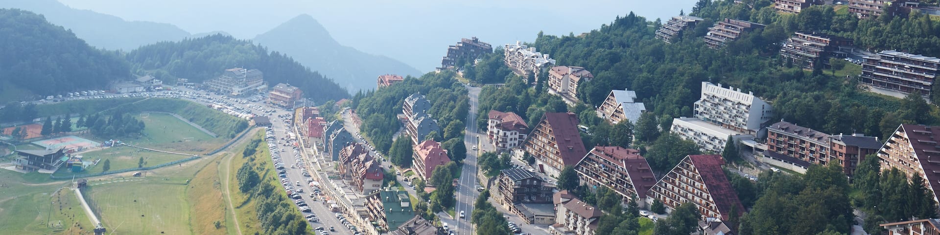 A mountainous town with terraced houses, a main road, and green fields.