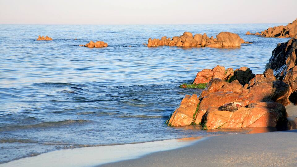A rocky shoreline with calm water and distant islands.