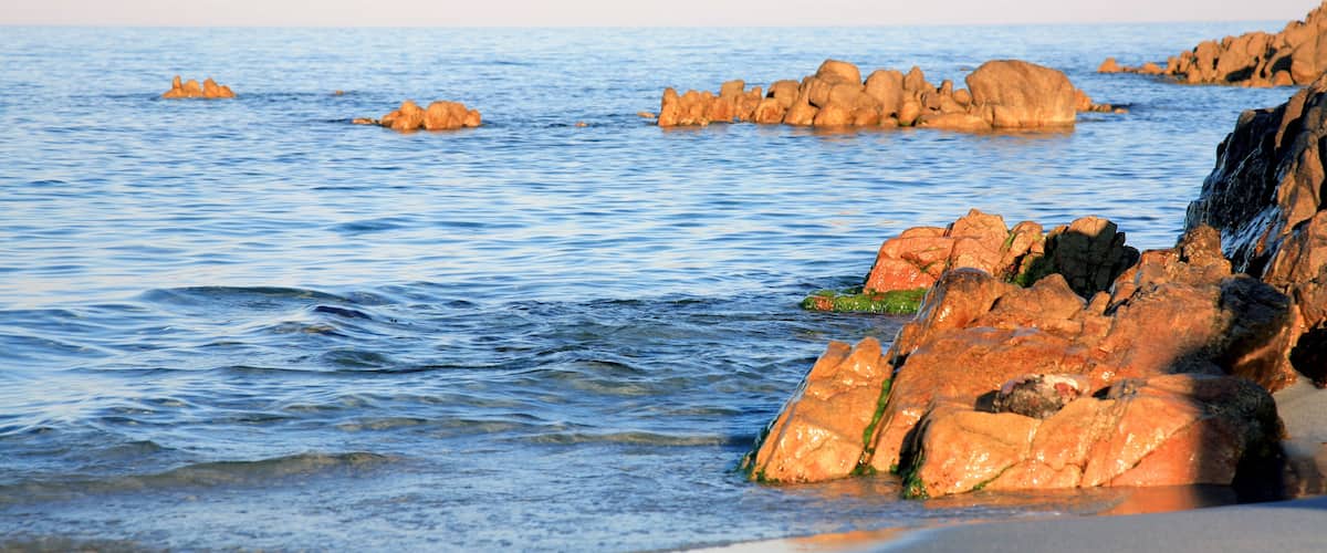 A rocky shoreline with calm water and distant islands.