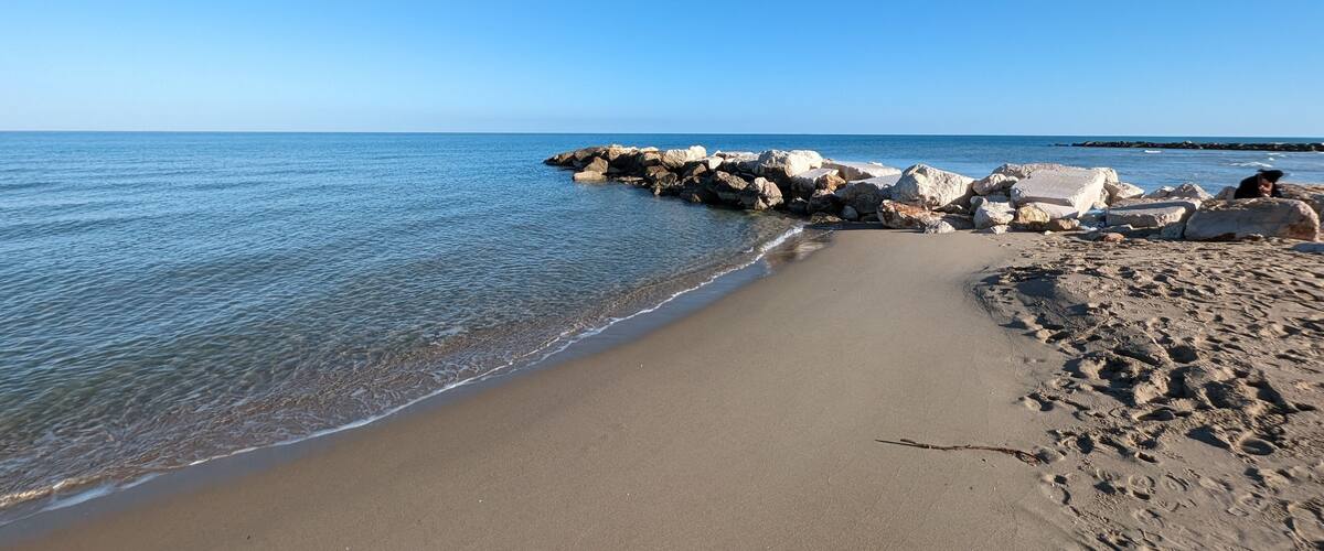 A sandy beach with large rocks and calm water.