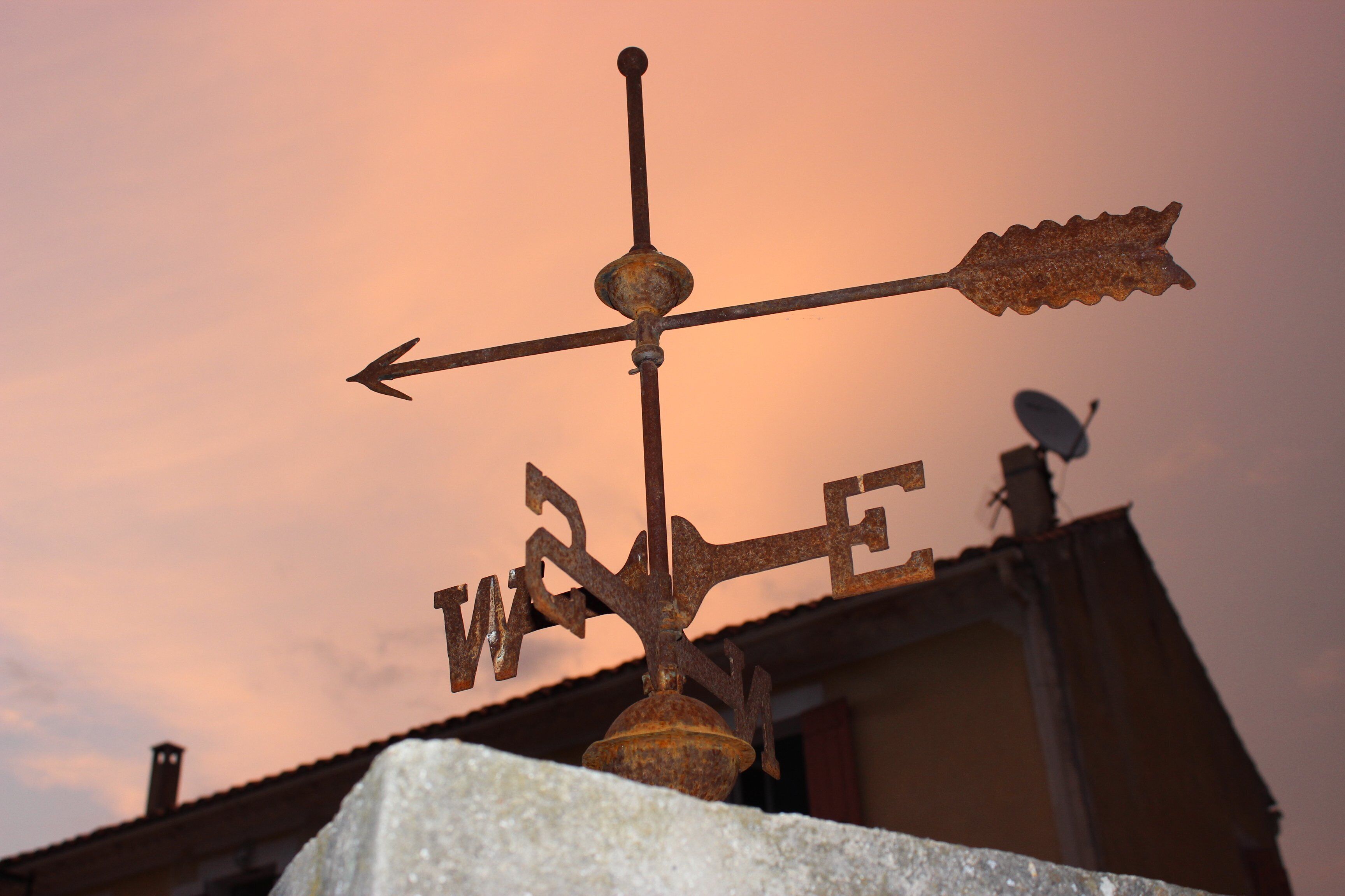 A weather vane with the word "WIND" on it, set against a sunset sky.