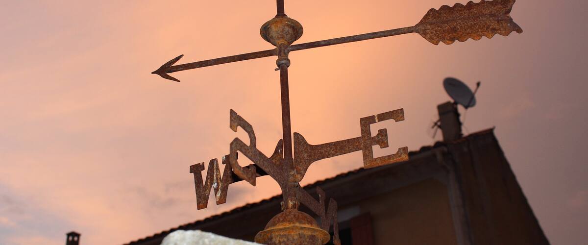 A weather vane with the word "WIND" on it, set against a sunset sky.