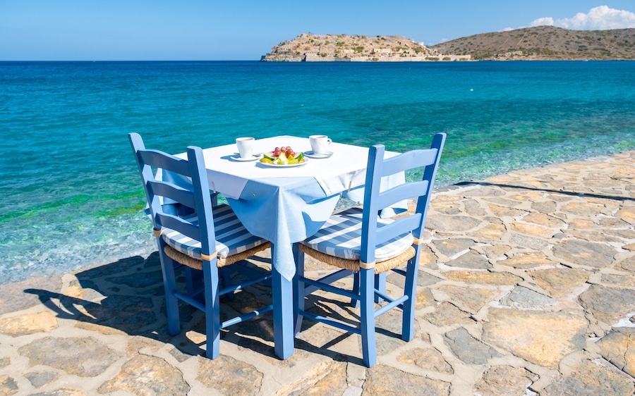 Una mesa con sillas frente al mar, con una costa rocosa y una isla distante.
