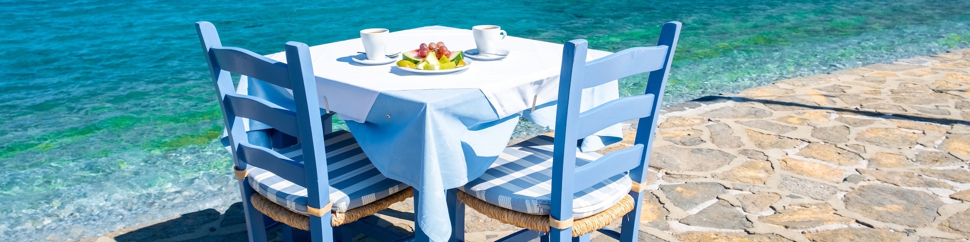 Una mesa con sillas frente al mar, con una costa rocosa y una isla distante.