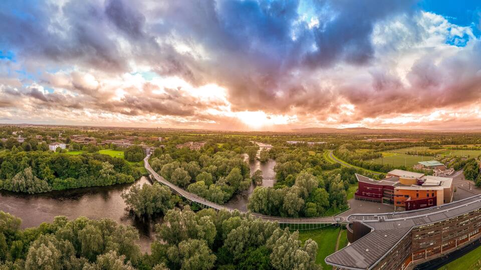 Aerial panoramic view of Living Bridge, curving modern pedestrian crossing over the Shannon river at the University of Limerick with stunning sunset