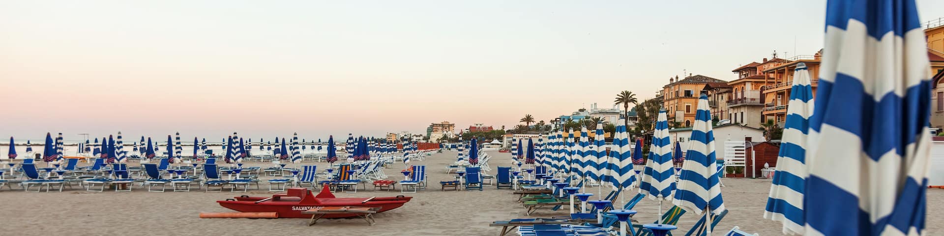 A beach with rows of blue and white striped beach umbrellas and lounge chairs.