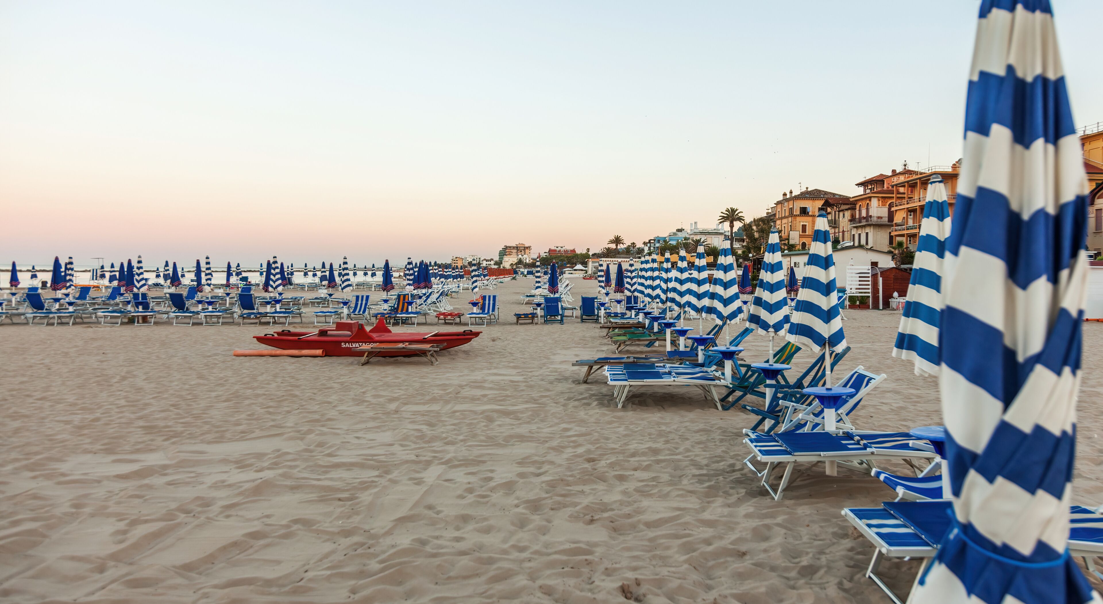 A beach with rows of blue and white striped beach umbrellas and lounge chairs.