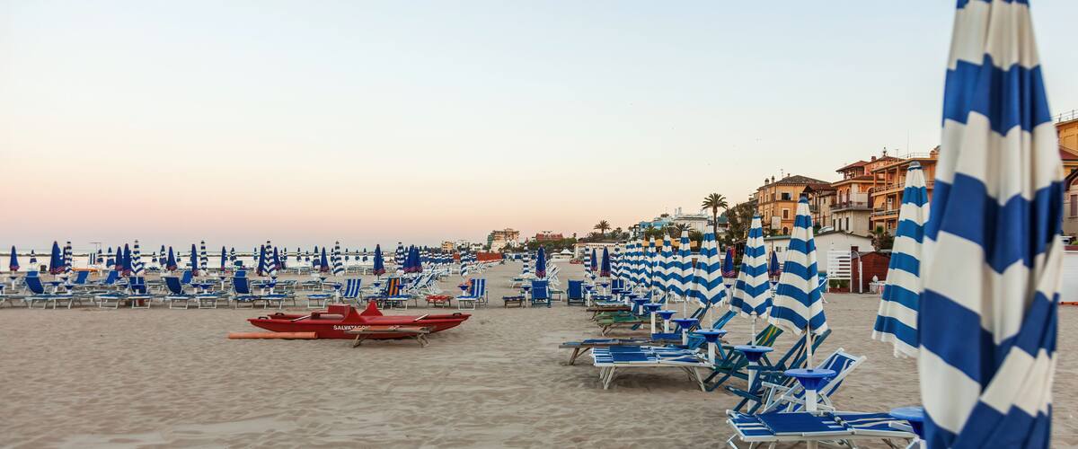A beach with rows of blue and white striped beach umbrellas and lounge chairs.