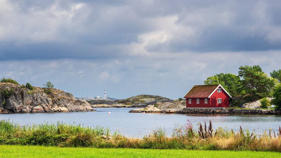 A red house by a lake with a lighthouse in the distance.