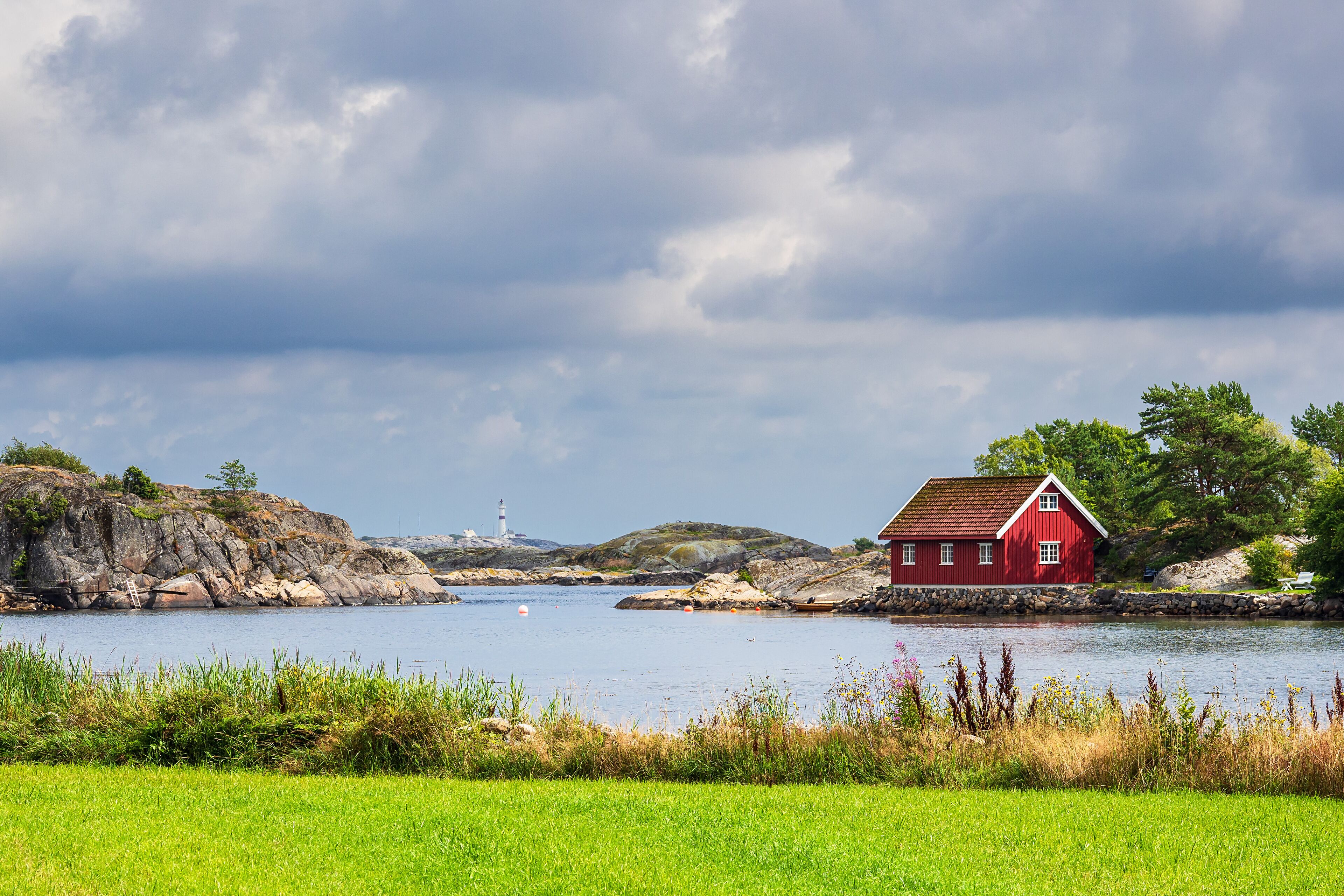 A red house by a lake with a lighthouse in the distance.