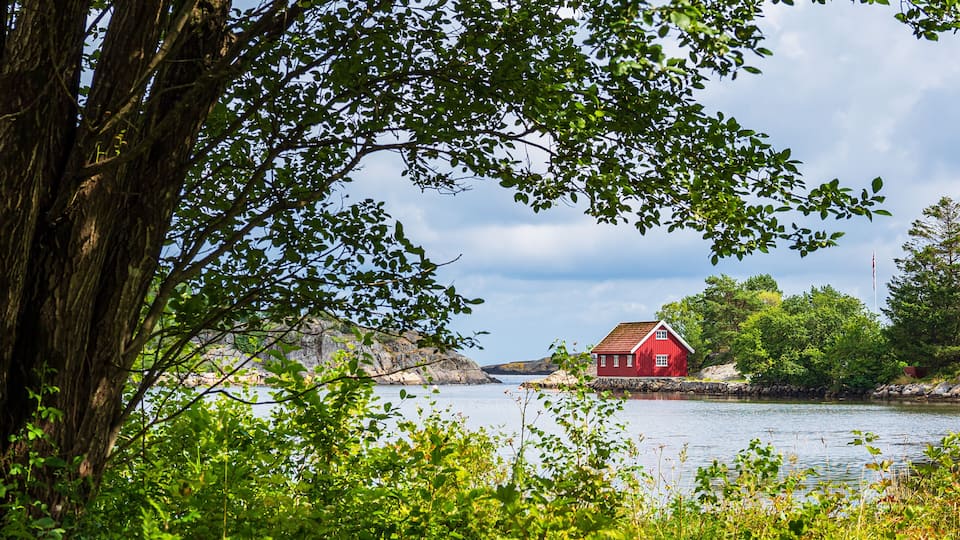 A red house by a calm lake surrounded by lush greenery and rocky terrain.