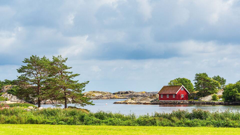 A red house by a lake with trees and rocks in the background.