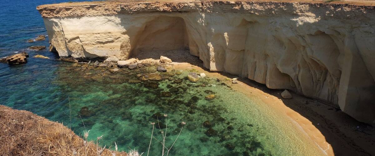 A coastal cliff with clear water revealing underwater vegetation.