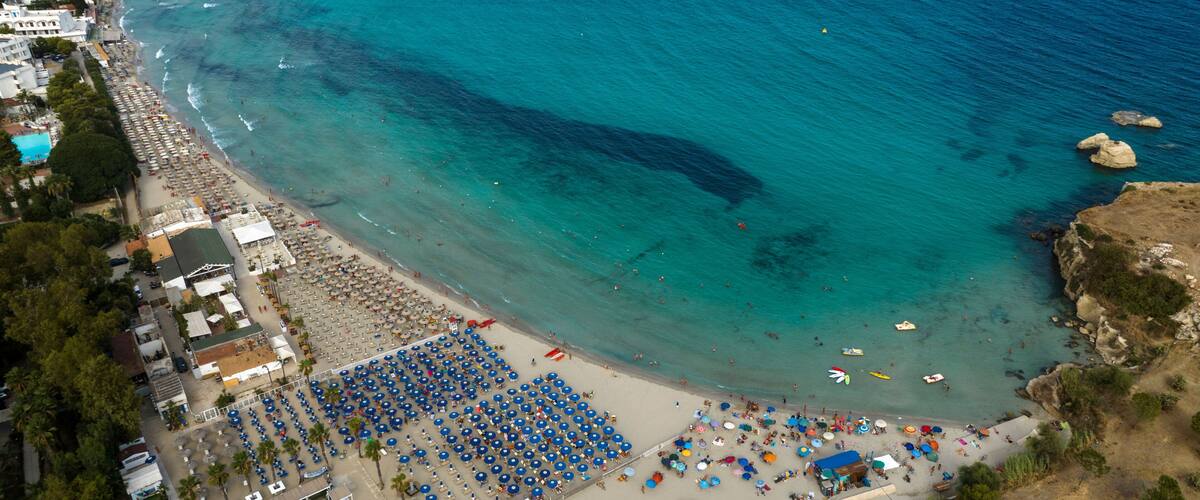 Aerial view of Fontane Bianche beach, located in the province of Syracuse, Sicily, Italy. There are many beach resorts with their umbrellas overlooking a blue, crystal-clear sea. It is a sandy beach.