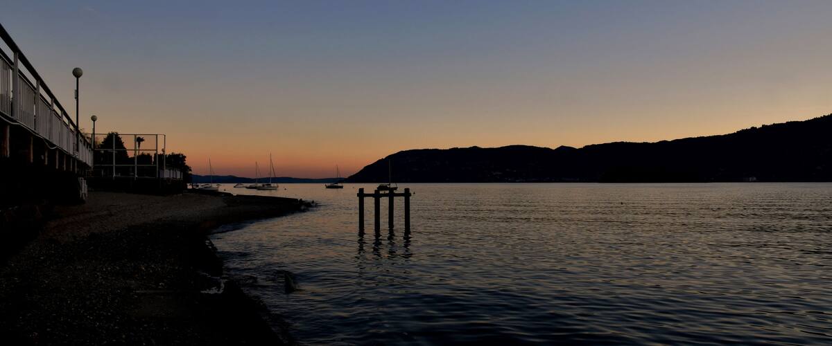 A sunset over a calm river with a pier and buildings on the left.