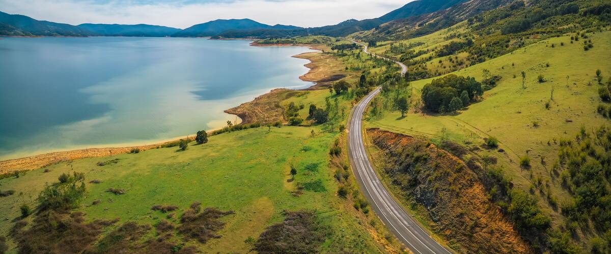 A winding road along a lake with mountains in the background.