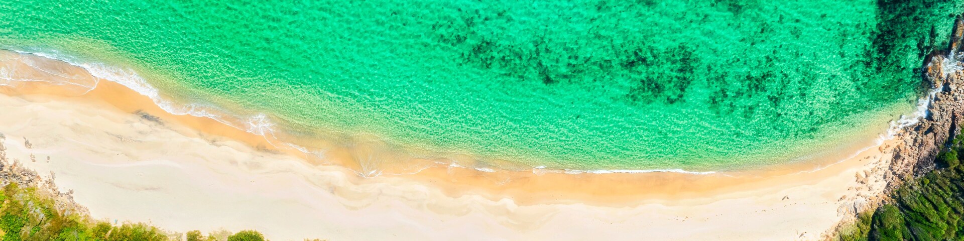 A turquoise beach with white sand, surrounded by dense green vegetation.