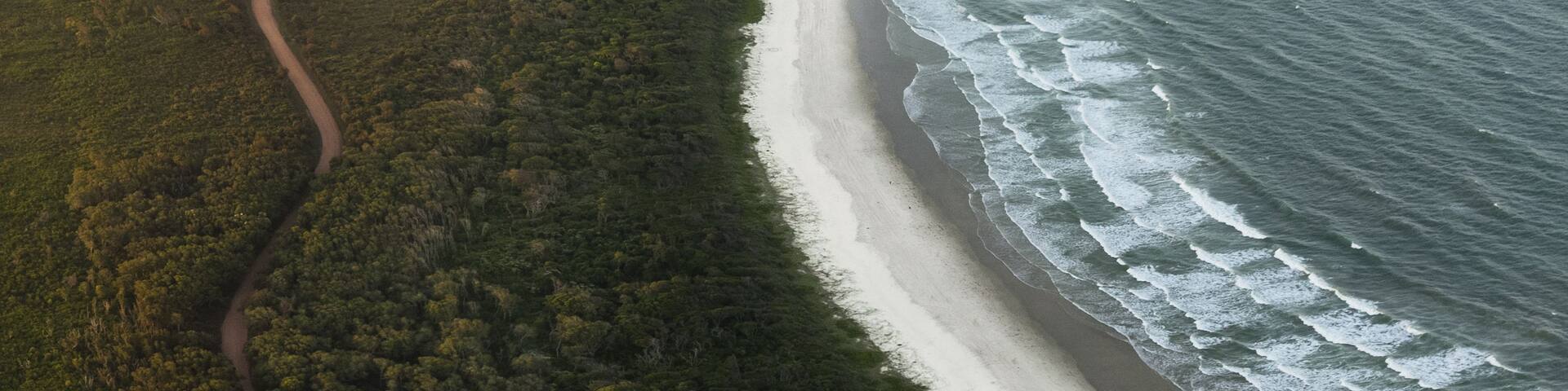 Aerial view of sunset glowing over the dark green forests meeting the white sand beach and turquoise waters at Diamond Head Beach, Crowdy Bay National Park, New South Wales, Australia.